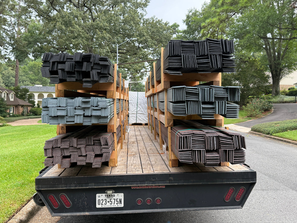 A flatbed truck loaded with stacks of Smooth Bender Board, photographed outdoors on a residential street with grass, trees, and houses visible in the background.
